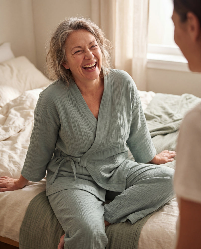 Customer photo placeholder — laughing with partner in bed, sage kimono